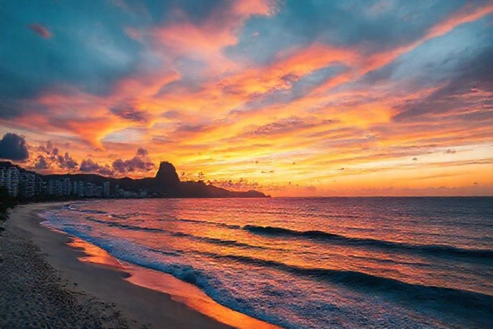 Pôr do sol na praia do Rio de Janeiro, refletindo as cores vibrantes no mar.