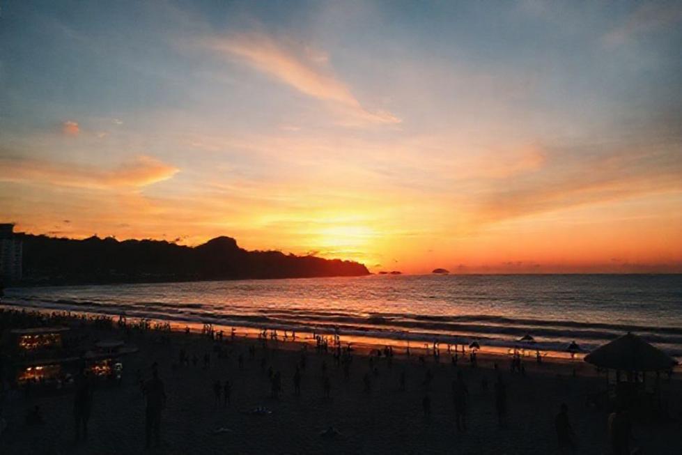 Pôr do sol na praia de Copacabana com pessoas aproveitando o momento.