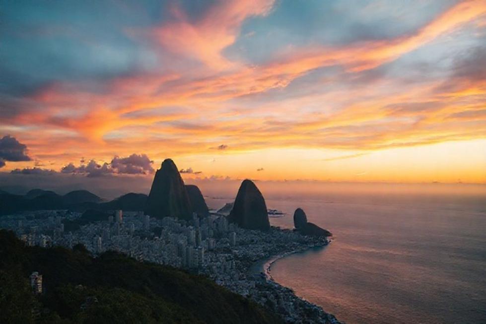 Pôr do sol sobre a cidade do Rio de Janeiro com contornos de montanhas ao fundo.