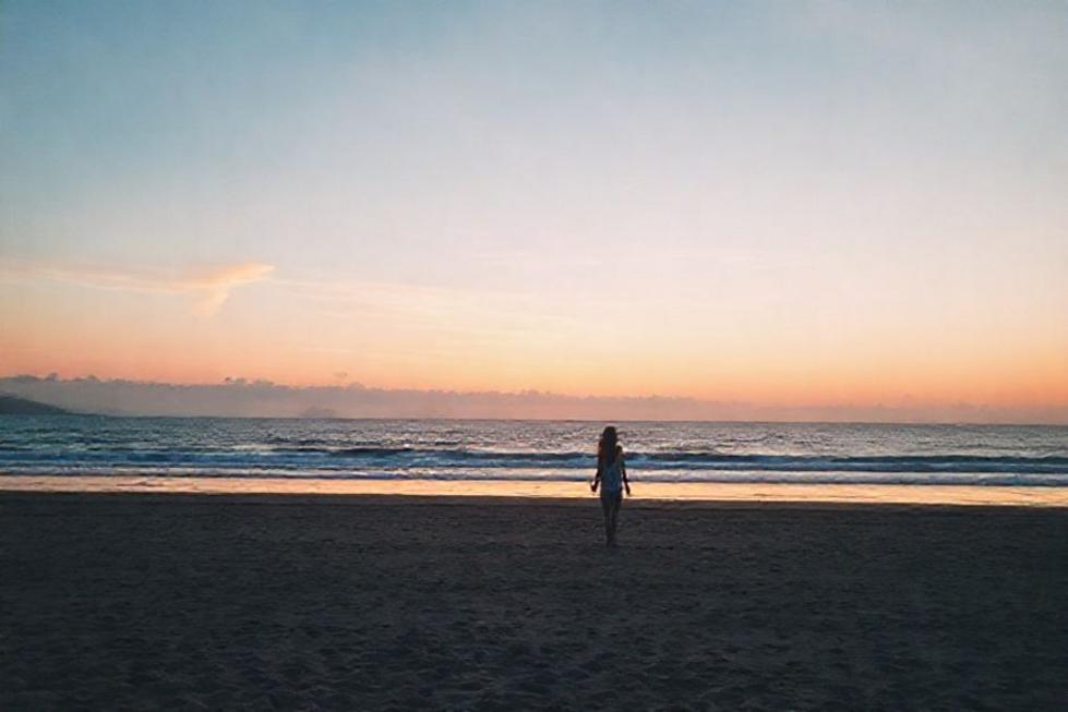 Pôr do sol romântico na praia de Florianópolis com um casal caminhando de mãos dadas.
